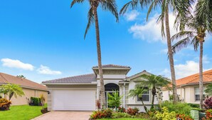 Una casa residenziale con garage, circondata da prati curati e palme.