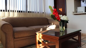 A living room with a brown sofa, a glass coffee table, and a vase with flowers. - Mar Sol (Mazatlán)