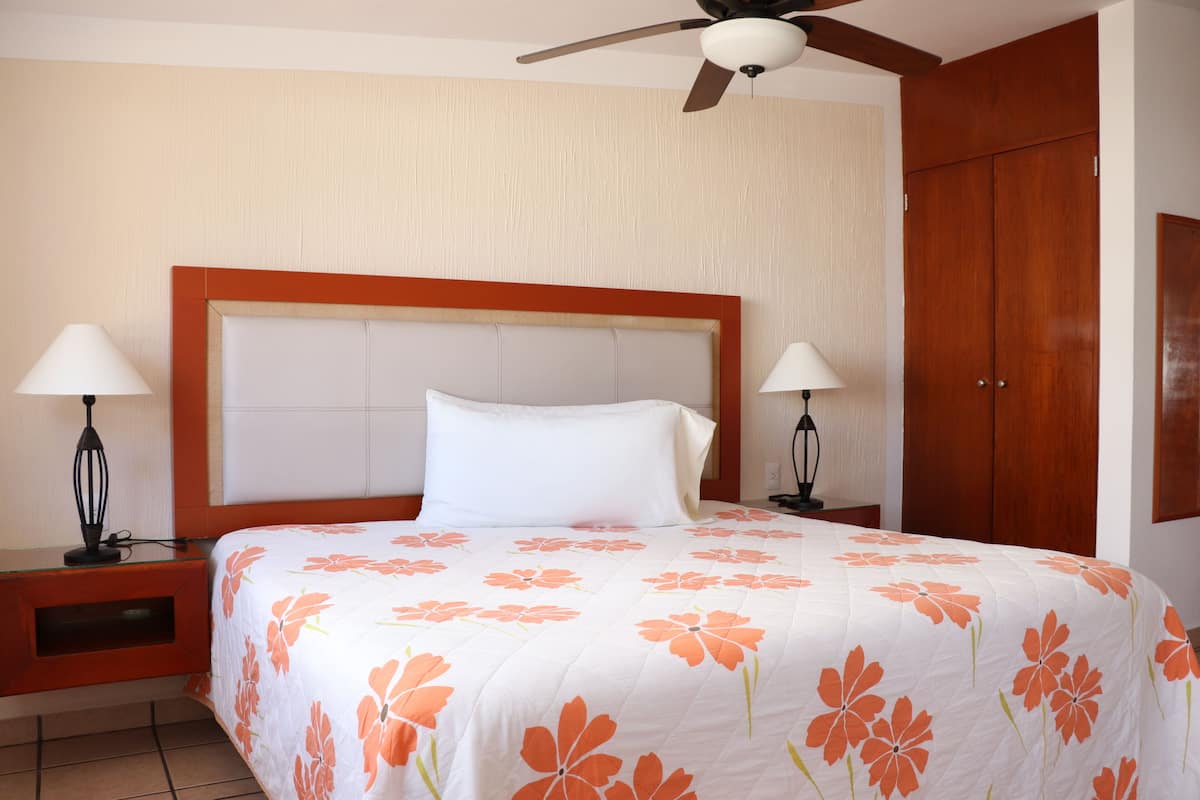 A hotel room with a large bed, two bedside tables with lamps, a wooden wardrobe, and a ceiling fan.