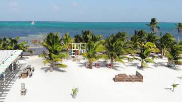 Une plage bordée de palmiers, un petit bâtiment et un bateau sur l’eau.