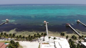 Een resort met bungalows boven het water, verbonden door looppaden, een strand en palmbomen.