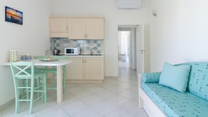 Cocina compacta con comedor, suelo de baldosas blancas y sofá color turquesa con cojines estampados.