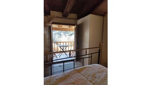 Ein Schlafzimmer mit einem Bett, einem Holgeländer und Blick auf einen Balkon mit Tisch und Stühlen.