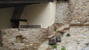 Ein gepflasterter Innenhof mit einer rustikalen Steinmauer, einem kleinen Bogen und einer Holzkonstruktion.