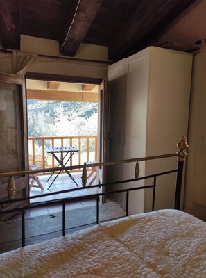 Een slaapkamer met een bed, een houten leuning en uitzicht op een balkon met een tafel en stoelen.