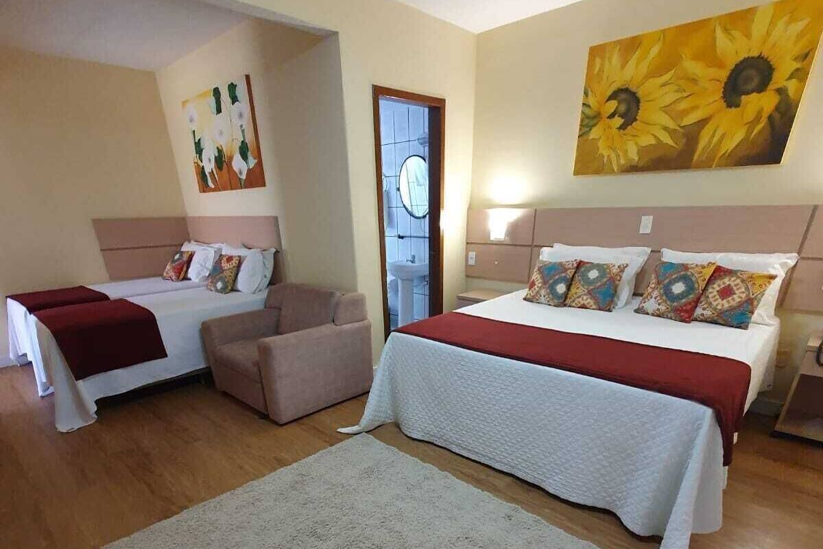 A hotel room with two beds, a sofa, a large rug, and a painting of sunflowers.