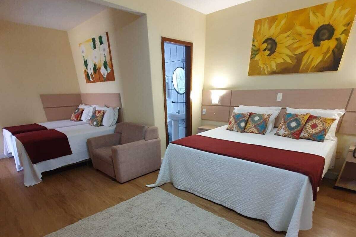 A hotel room with two beds, a sofa, a large rug, and a painting of sunflowers.