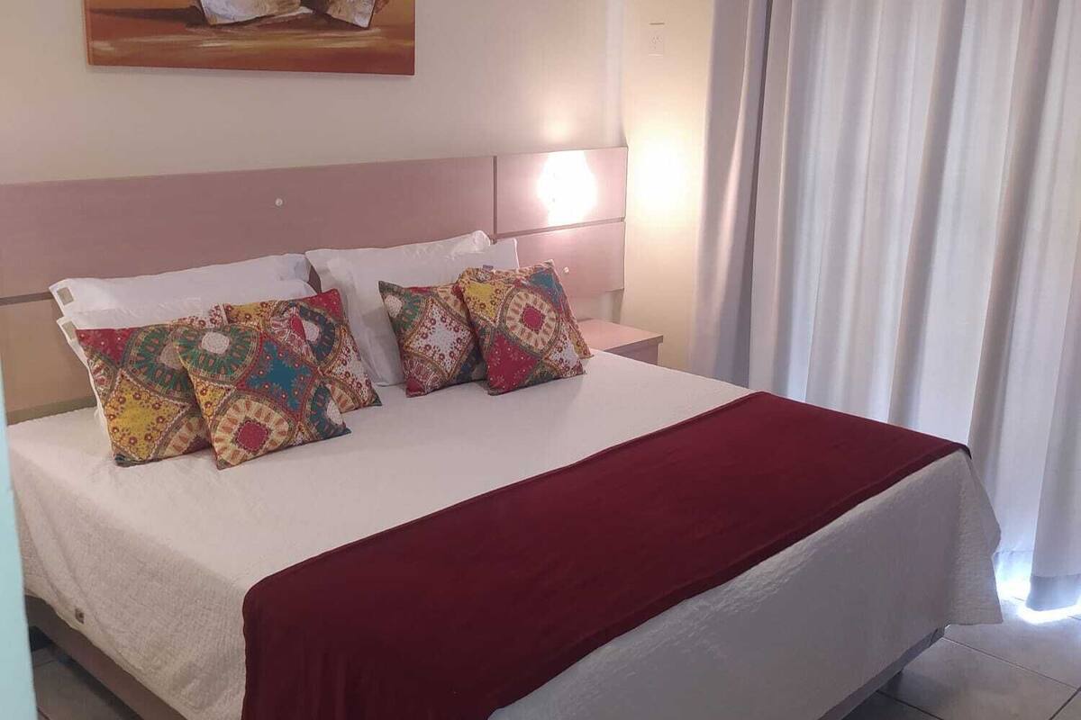 A neatly made bed with a red blanket, a headboard, and multiple patterned pillows.