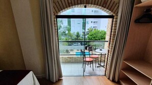 A hotel room with a large sliding glass door leading to a balcony with a pool, outdoor seating, and a view of buildings and greenery. - Hotel João de Barro (Itajai)