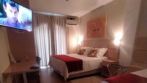 A hotel room with two beds, a desk, a TV, and a large window with curtains. - Hotel João de Barro (Itajai)