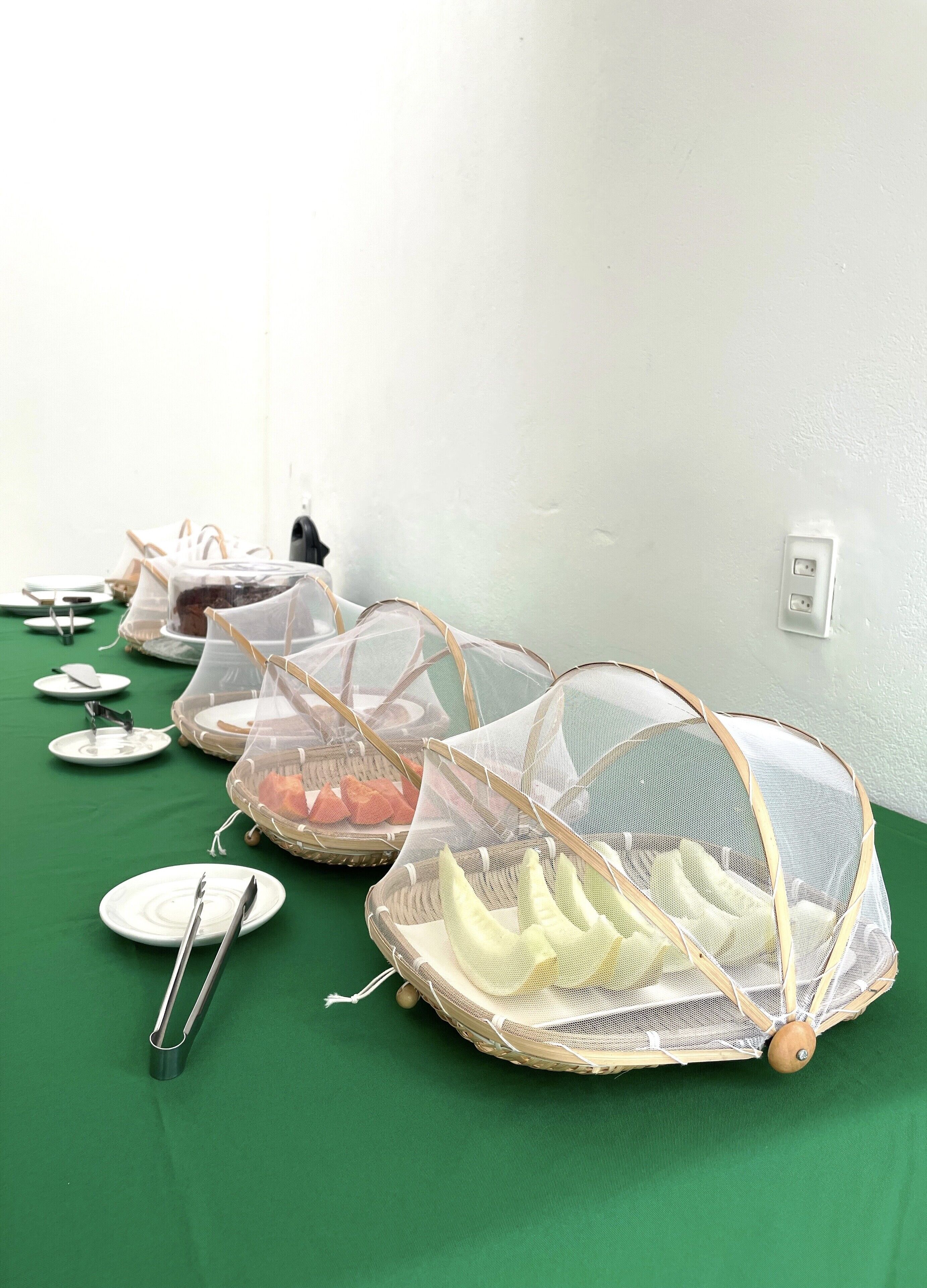 Una mesa de buffet con cestas de comida cubiertas y utensilios sobre un mantel verde.