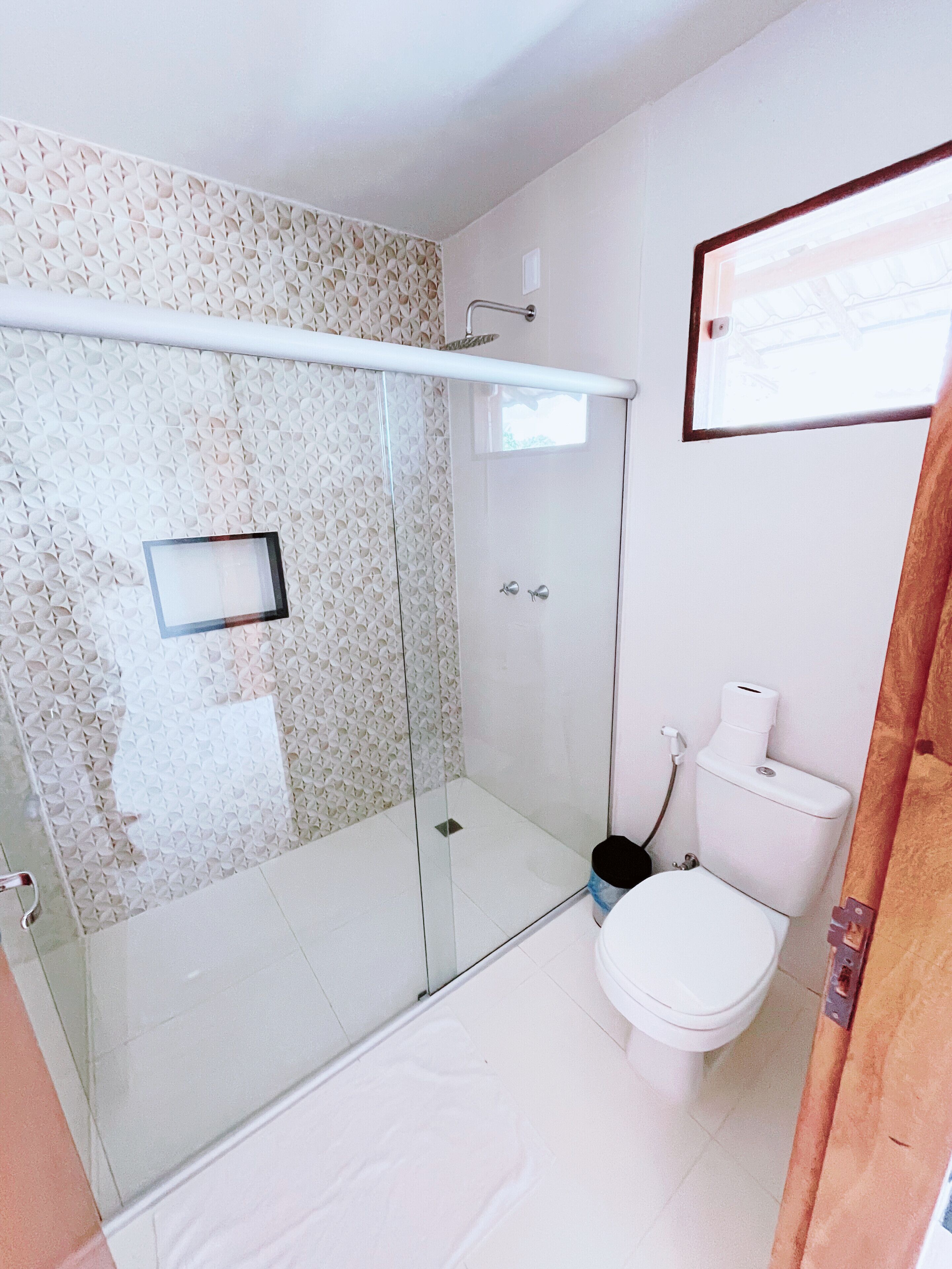 Un baño con ducha, inodoro y un ventanal pequeño.