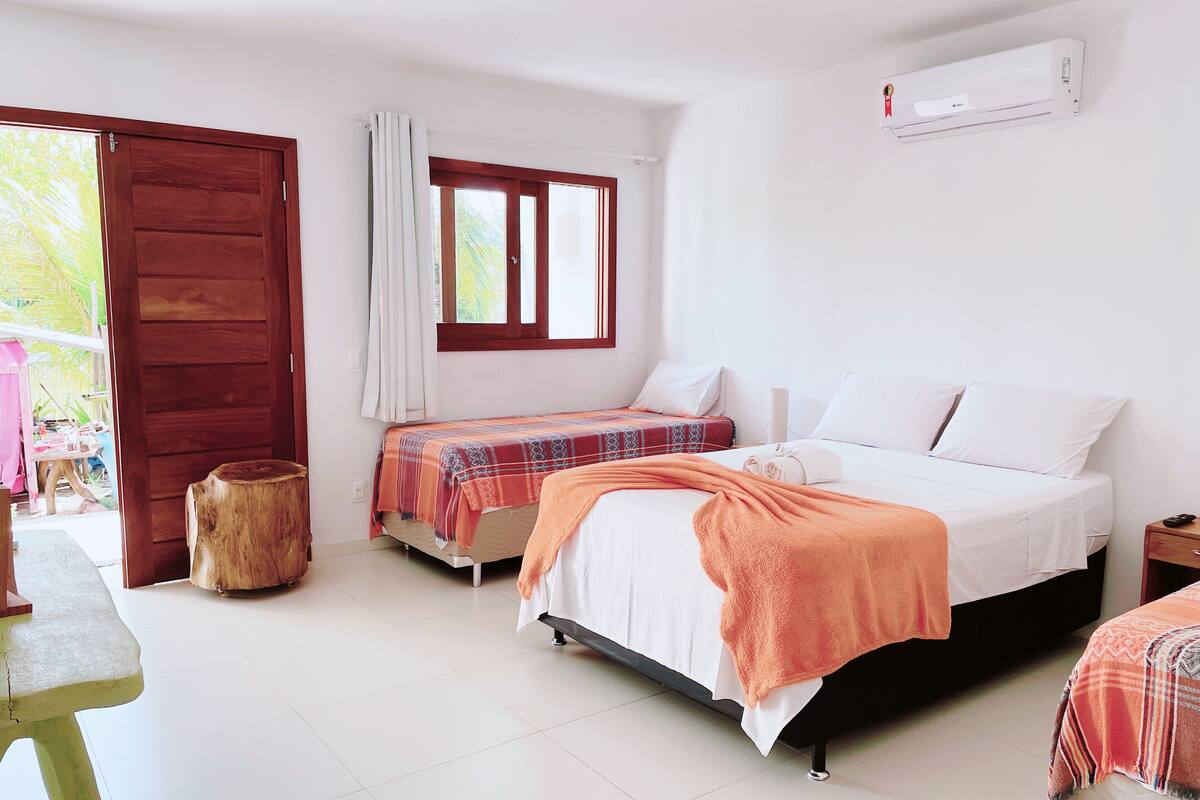 A bedroom with two beds, a wooden stool, a table, and a window with curtains.