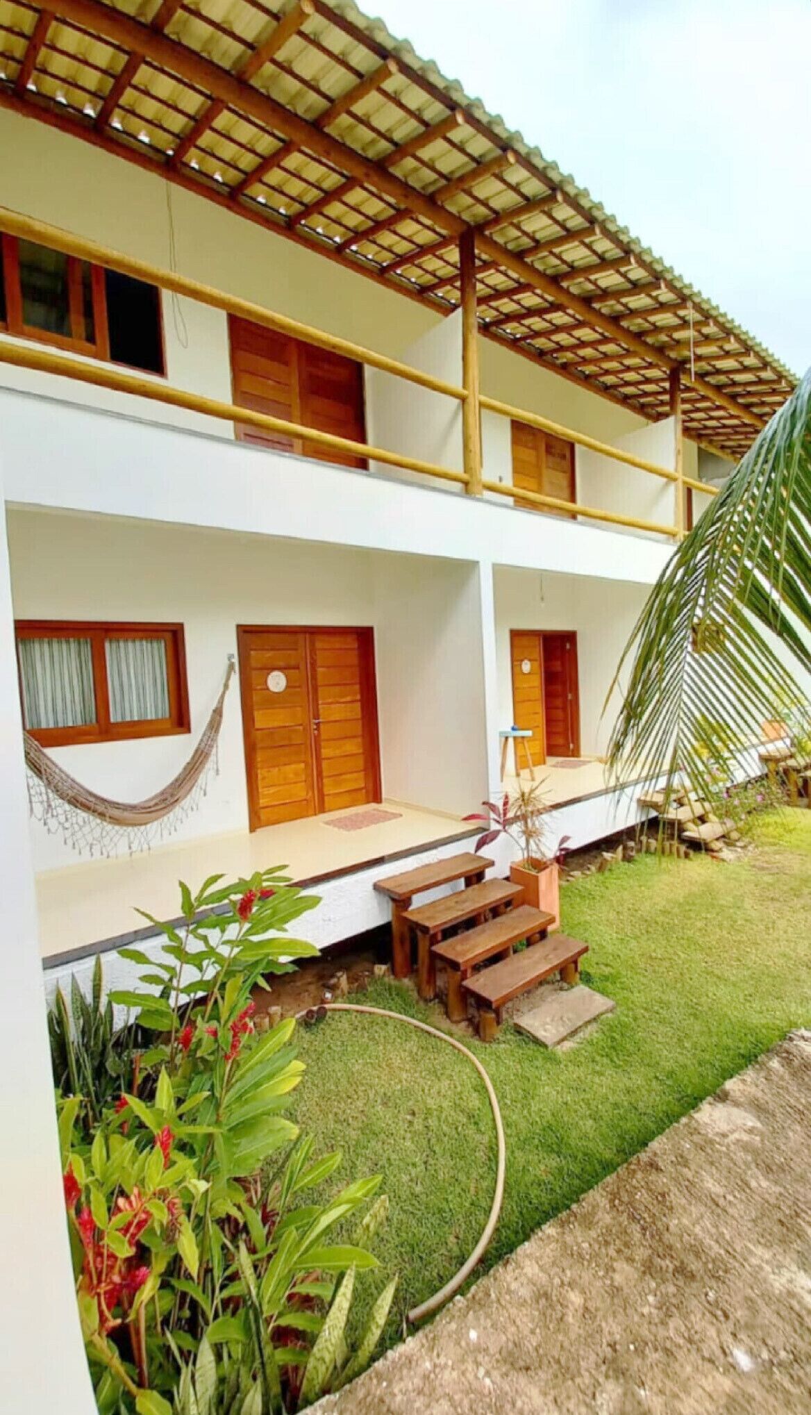 A two-story building with a wooden balcony, a hammock, and a small garden area with benches.