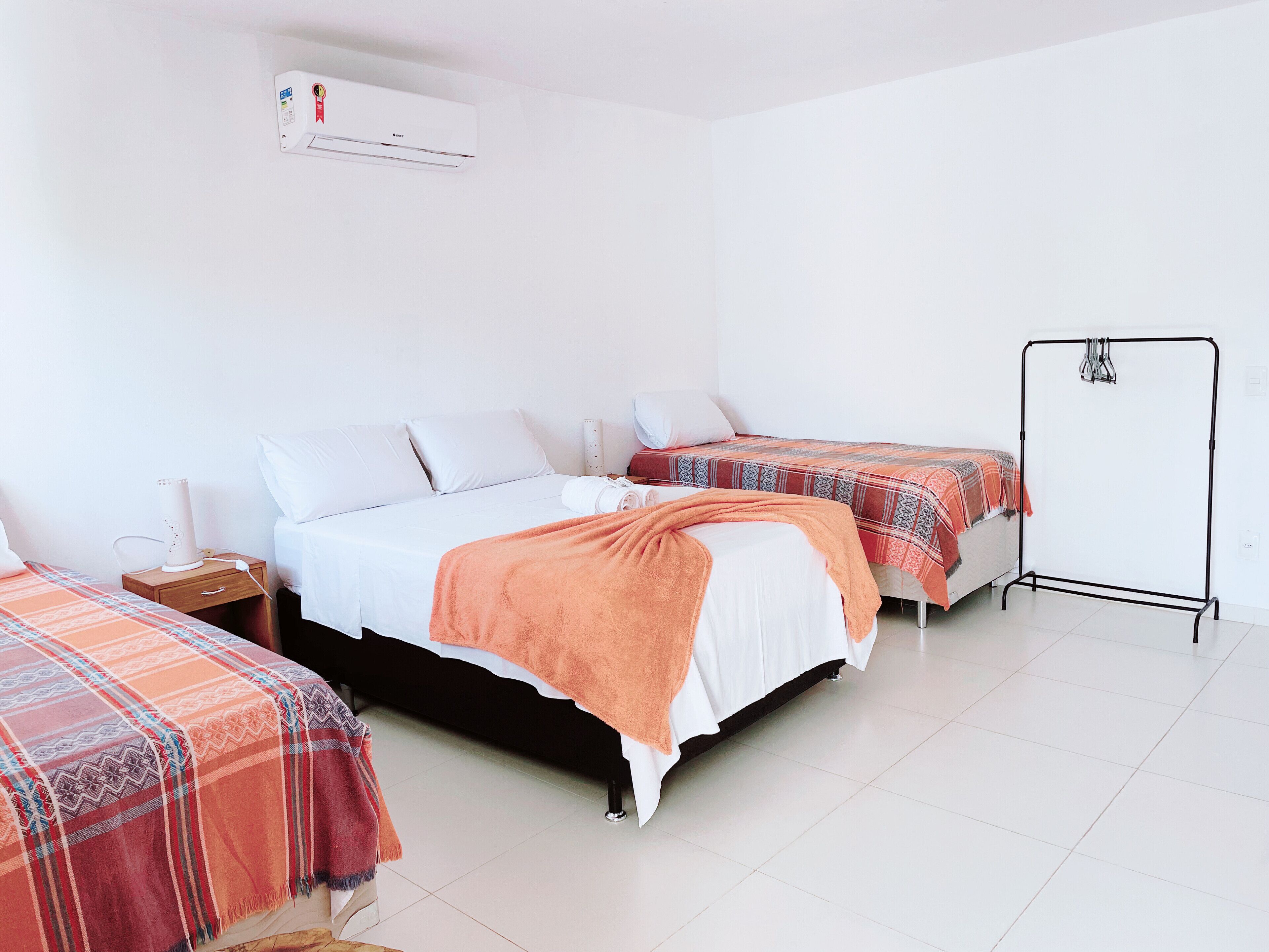 A hotel room with two beds, a wardrobe, a bedside table, and an air conditioning unit.