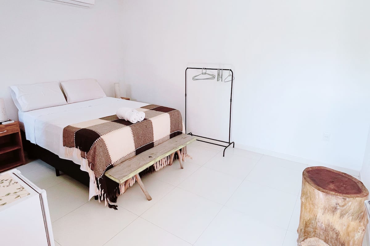 A bedroom with a bed, a wooden bench, a clothing rack, and a wooden stool.