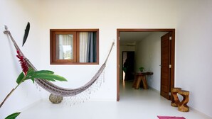 Una habitación con una hamaca, una mesa de madera con una planta y una puerta que da a otra habitación.
