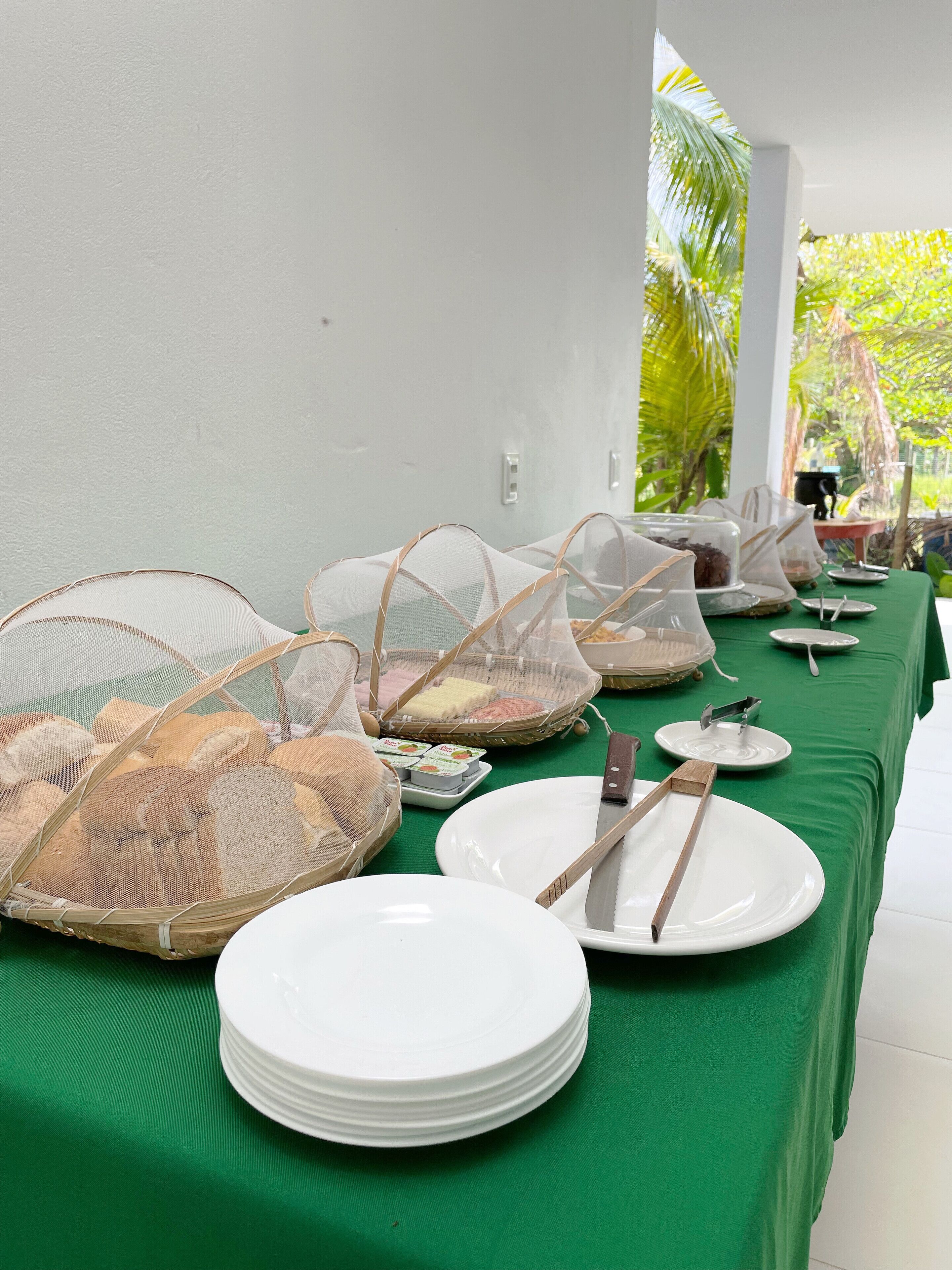 A buffet table with white plates, bowls, and utensils, covered by a green tablecloth.