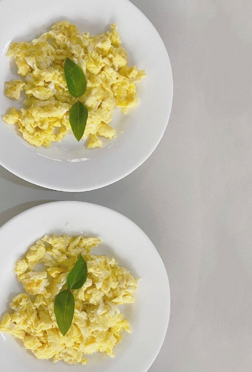 Two white plates of scrambled eggs with a green leaf garnish.