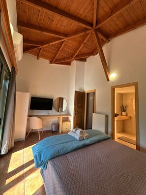 A bedroom with a wooden ceiling, a bed with blue and brown bedding, a desk with a computer, a chair, and a small plant.