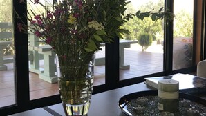 Ein Zimmer mit großem Fenster, einer Blumenvase, einem Tablett mit Kerzen und einem Buch auf einem Tisch.