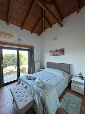Ein Schlafzimmer mit Bett, Sitzbank, Nachttisch und Blick durch eine Glastür.