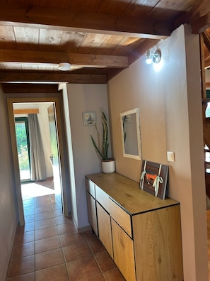 A hallway with wooden ceiling beams, a potted plant, and framed artwork on the wall.