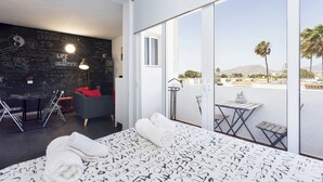 A modern hotel room with a large bed, a desk, a chair, a small table, a sofa, and a balcony with a view. - Home2Book Modern Studio & Pool Costa del Silencio (Arona)