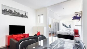 A modern hotel room with a cityscape artwork, a flat-screen TV, a dining table, and a bed with a city view. - Home2Book Modern Studio & Pool Costa del Silencio (Arona)