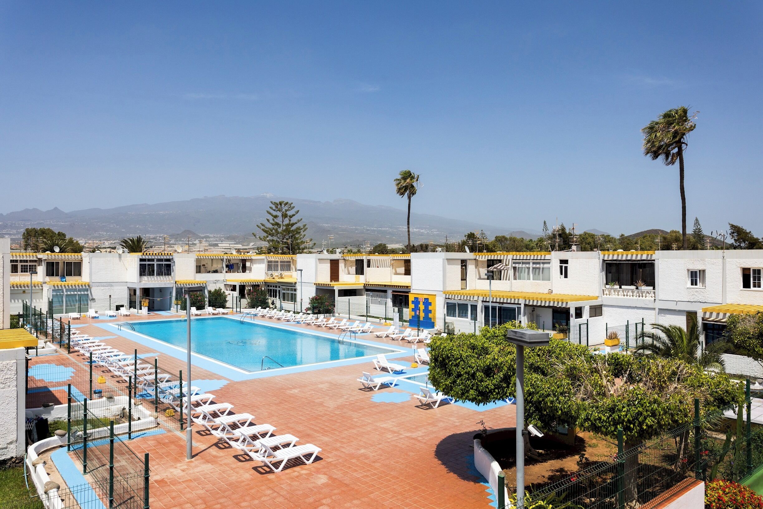 Un albergo con piscina, lettini prendisole e vista sulle montagne lontane.