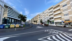 A street view with a modern building on the left, a clear blue sky, and a road with directional arrows.