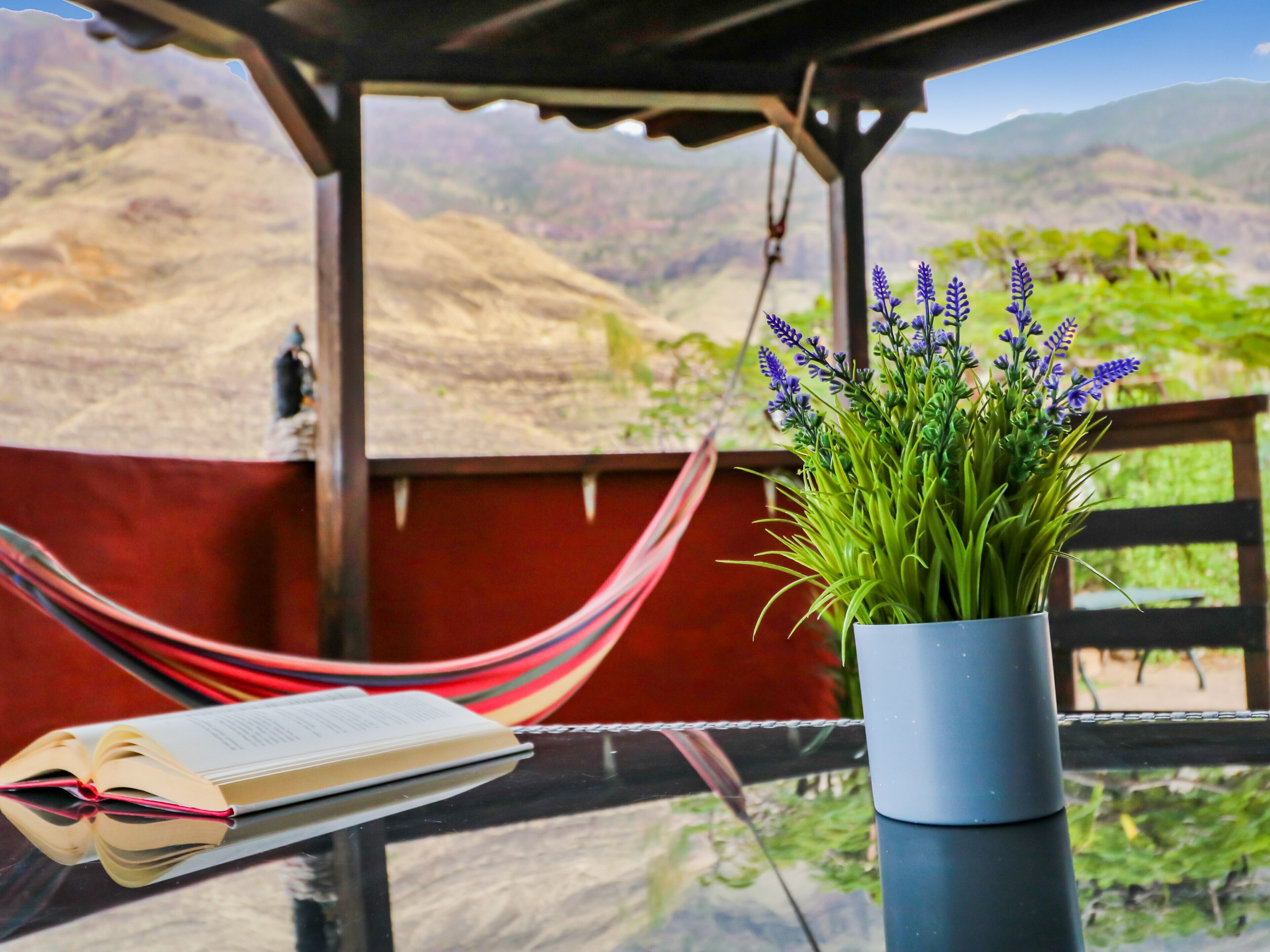 A hammock, a book, and a potted plant with lavender on a balcony with a mountain view.