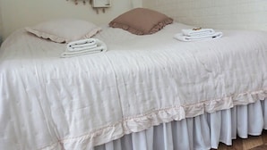 A bed with a white bedspread and ruffled hem, two pillows, and a small bedside table with a plant. - Apartament Mickiewicz - Center Wi-Fi, TV, Netflix, Parking (Slupsk)