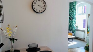 A modern dining area with a wooden table, black placemats, and a wall clock. - Apartament Mickiewicz - Center Wi-Fi, TV, Netflix, Parking (Slupsk)