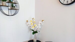 A dining area with a wooden table, black placemats, a vase with flowers, a black bowl, and a wall clock. - Apartament Mickiewicz - Center Wi-Fi, TV, Netflix, Parking (Slupsk)