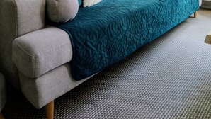 A grey sofa with teal and white cushions, a teal throw blanket, and decorative wall art. - Apartament Mickiewicz - Center Wi-Fi, TV, Netflix, Parking (Slupsk)
