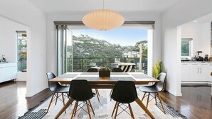 A modern dining area with a large table, black chairs, and a view of a hillside. - West Hollywood Hills Pool Home With Views (Los Angeles)