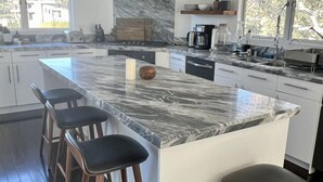 A modern kitchen with a large island, bar stools, a built-in oven, and a large window. - West Hollywood Hills Pool Home With Views (Los Angeles)