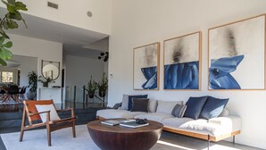A modern living room with a sofa, coffee table, and a dining area with chairs. - West Hollywood Hills Pool Home With Views (Los Angeles)
