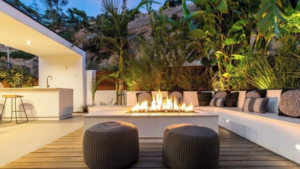 A modern outdoor seating area with a fire feature, a bar, and lush tropical plants. - West Hollywood Hills Pool Home With Views (Los Angeles)
