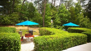 Un patio con dos sombrillas azules, una parrilla y una mesa.