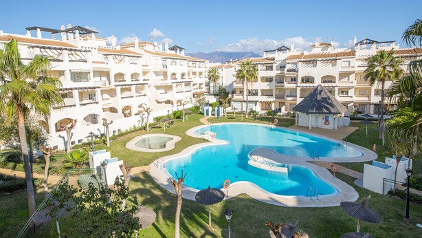 Um resort com uma piscina grande, várias varandas e palmeiras.