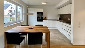 Moderni keittiö, jossa on valkoiset kaapit, puinen ruokapöytä ja mustat tuolit.