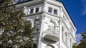 Un bâtiment blanc à l’architecture classique, avec des balcons richement décorés et des fenêtres en arc de cercle.