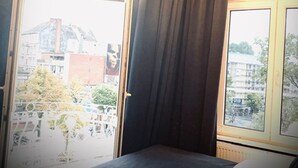 Une chambre avec un lit, de grandes fenêtres avec des rideaux et un lustre.