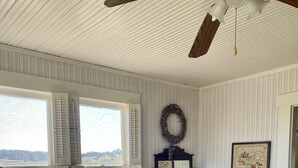 Une pièce avec une grande fenêtre, un banc en bois, une commode, un miroir et une couvre-lit matelassé.
