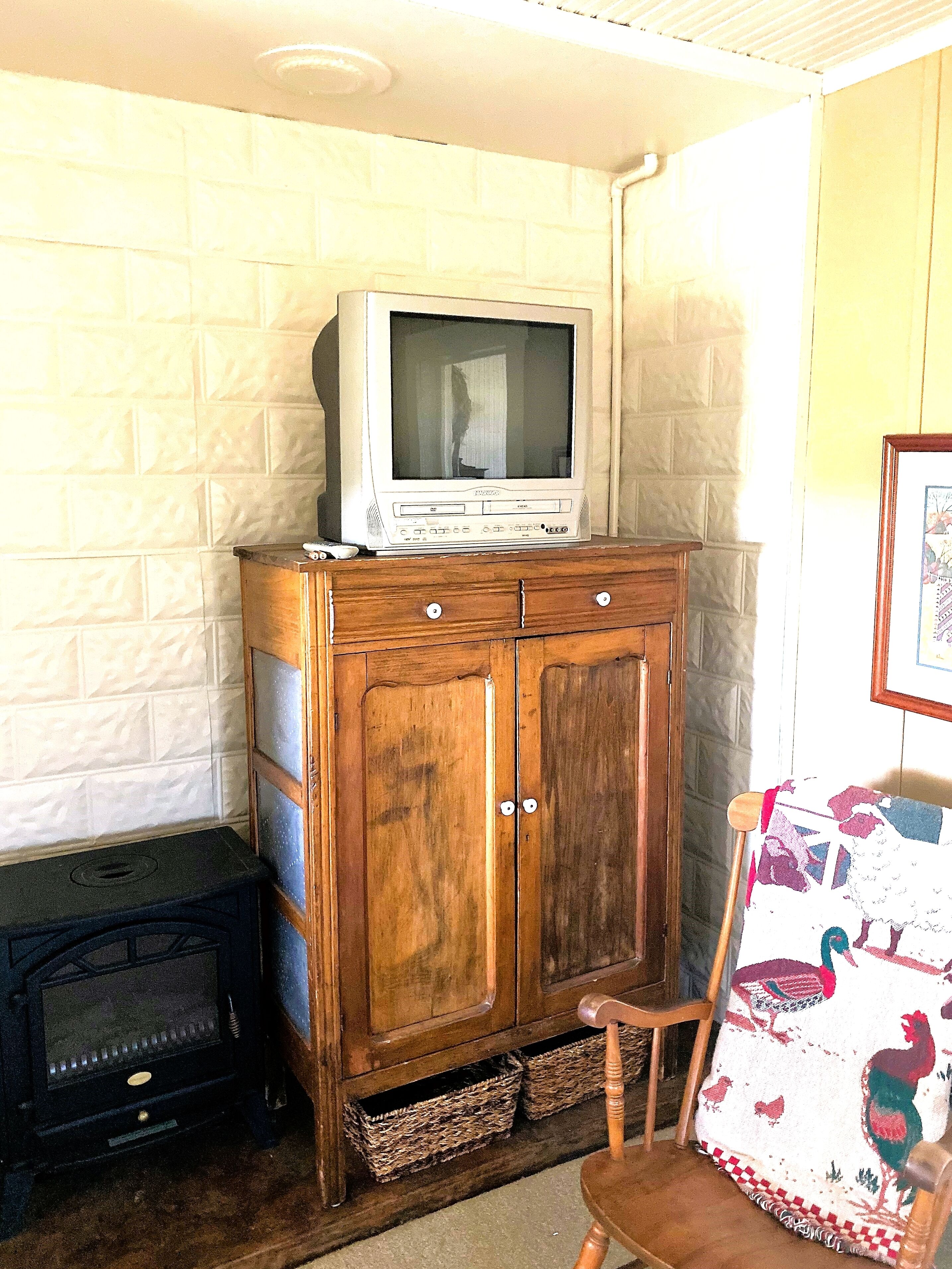 Een houten kast met een televisie erboven, een stoel met een sprei en een open haard.