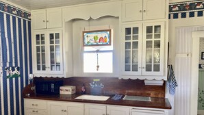 Une cuisine avec des meubles blancs, un plan de travail en bois, une fenêtre ornée de vitraux et un petit évier.