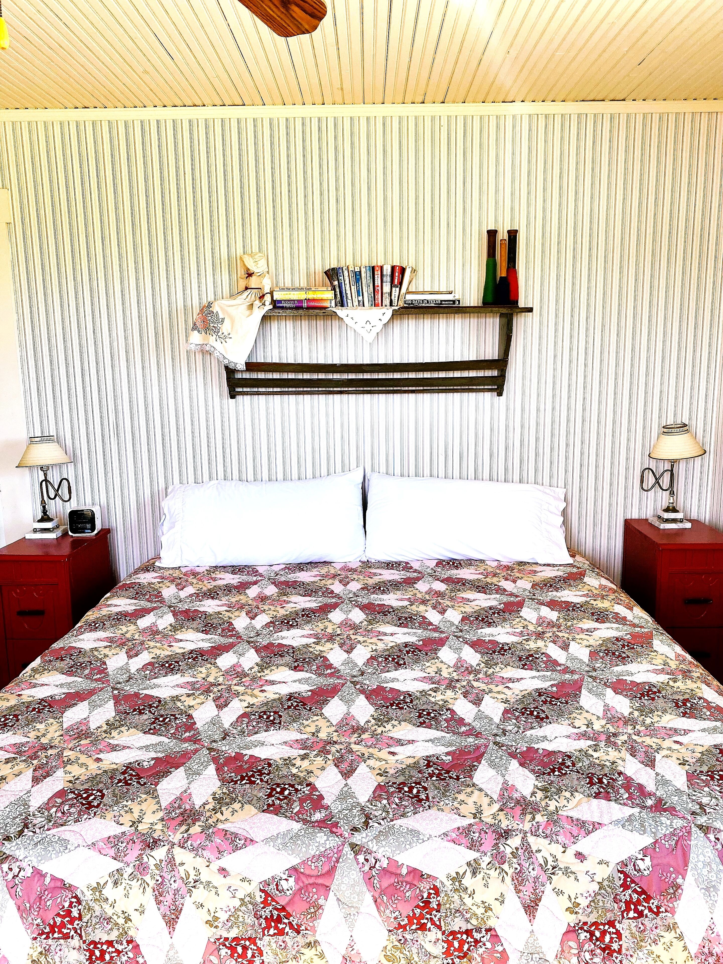 A room with a bed, a shelf with books, two bedside tables with lamps, and a striped wall.