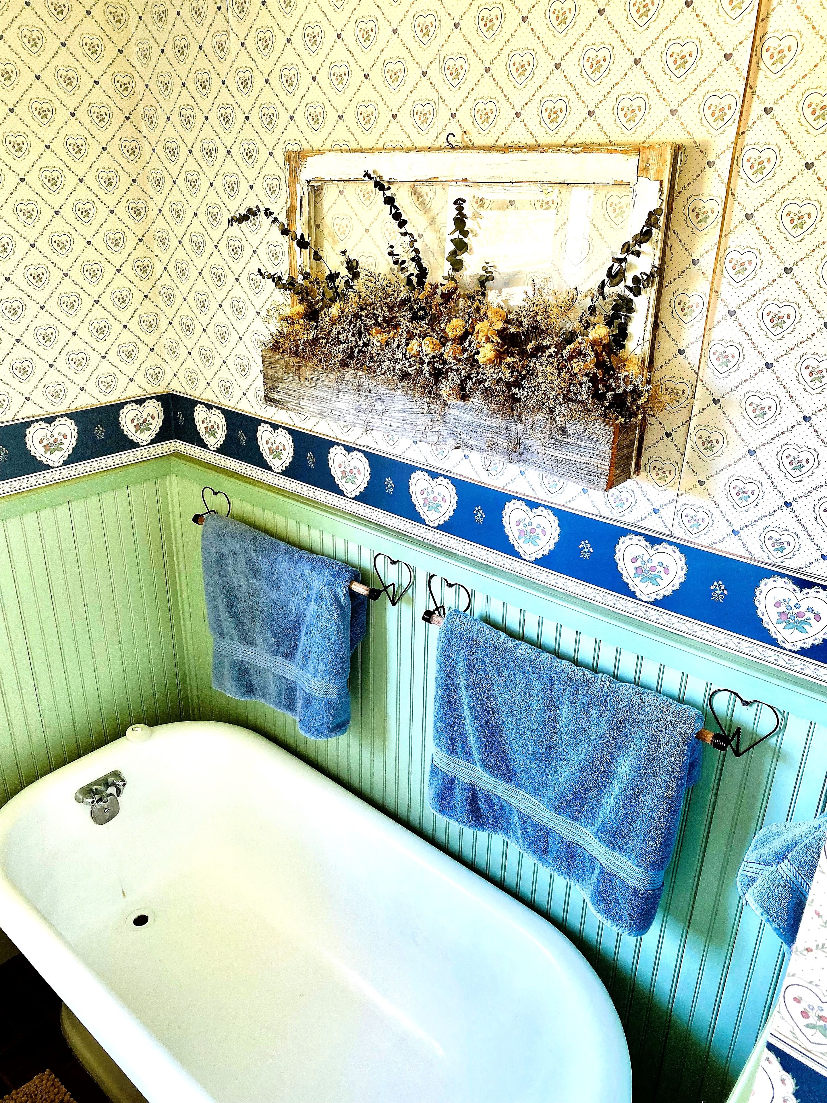 A bathroom with a bathtub, two towels hanging on heart-shaped hooks, and a mirror above the tub.
